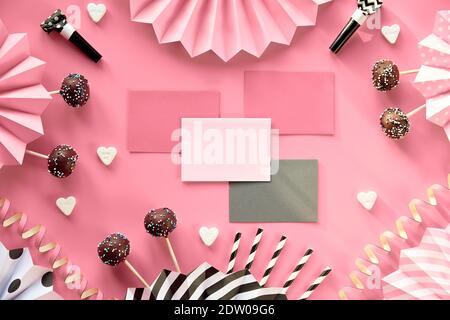 Schede di invito con spazio di copia. Torte al cioccolato decorate con glassa di zucchero colorata. Carta fotografica monocromatica piatta creativa su carta rosa con carta piegata Foto Stock