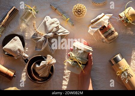 Piatto con zero rifiuti regali di Natale. La mano tiene la tazza di caffè in movimento. Regalo di Natale avvolto in asciugamano, tazze di bambù e fiasca. I regali sostenibili su Foto Stock