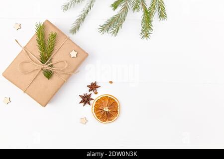 Composizione di Natale piatto - scatole regalo decorate con rami di abete, arance secche e spezie su sfondo bianco di legno. Foto Stock