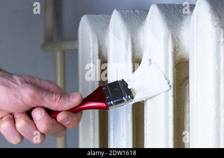 Verniciatura di un radiatore in ghisa con una spazzola di colore bianco. Concetto di rinnovamento. Foto Stock