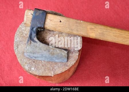 Un'ascia rimane su un pezzo di legno con sfondo rosso tappeto. Foto Stock