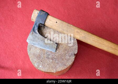 Un'ascia rimane su un pezzo di legno con sfondo rosso tappeto. Foto Stock