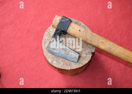 Un'ascia rimane su un pezzo di legno con sfondo rosso tappeto. Foto Stock