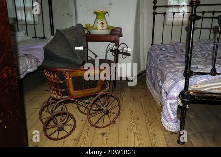 Passeggino antico d'epoca in camera da letto scura di vecchio stile, con due vecchi letti e coperte Foto Stock