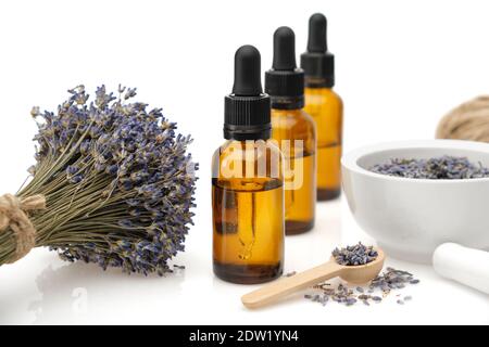 Tre bottiglie di olio essenziale di lavanda o di acqua di fiori aromatici, mortaio e mazzo di fiori di lavanda essiccati su sfondo bianco. Foto Stock