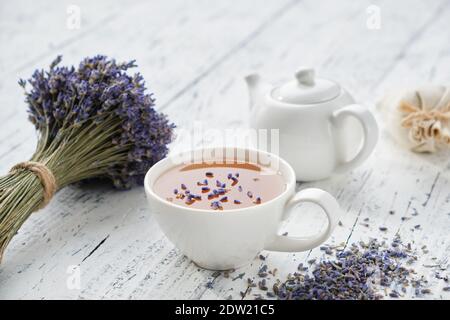 Tisana di lavanda sana, fiori secchi di lavanda e bollitore per tè su tavolo di legno bianco. Foto Stock