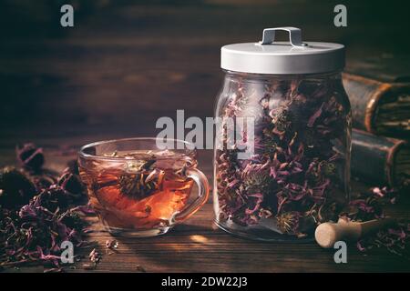 Tazza di sano tè echinacea, vaso di vetro di erbe secche di coneflower e vecchi libri sul tavolo. Foto Stock