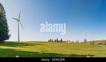 Turbine eoliche multiple in collina con cielo blu e idilliaco fattoria Foto Stock