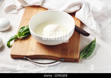 Palla di mozzarella in un recipiente e foglie di basilico fresco. Foto Stock