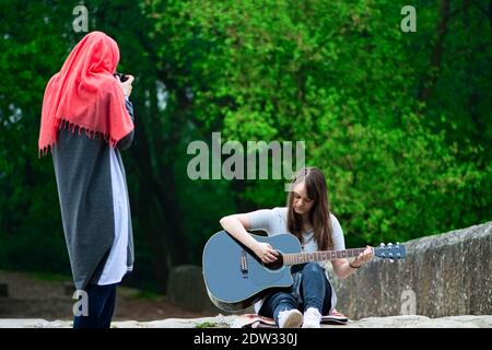 Ragazza musulmana che scatta foto di giovane ragazza mentre suona la chitarra Foto Stock