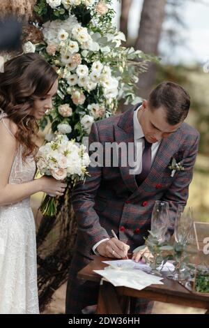 Sposi le carte di cerimonia nuziale firmanti e la sposa che lo guarda alla cerimonia nuziale. Buon sposi novelli Foto Stock