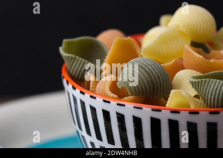 Una ciotola con pasta italiana a forma di lumache conosciuto come conchiglie in più colori con spazio di copia Foto Stock