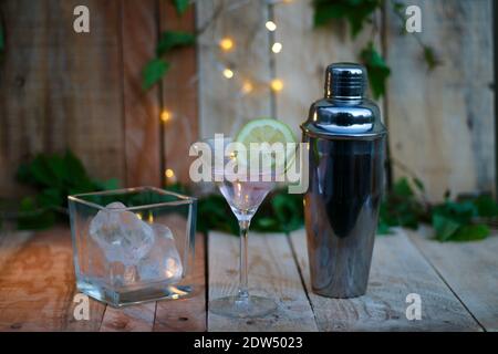 shaker con limoni di ghiaccio di vetro su sfondo di legno e foglie Foto Stock