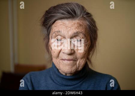 Donna carina più anziana di novanta anni caucasica con capelli grigi e rughe volto guarda la macchina fotografica, carino aspetto gentile e sorriss.Maturo nonna ritirata Foto Stock