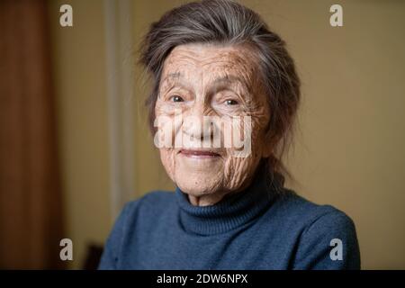 donna anziana carina di 90 anni con capelli grigi e rughe viso, indossando maglione, ritratto grande, sorridente e guardando gioiosamente, sfondo di stanza. Th Foto Stock