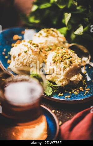 Dolce turco tradizionale semola helva. Scoop di helva di semola dolce con pistacchio noci, menta fresca e tè turco in piatto sopra il tavolo arrugginito b Foto Stock