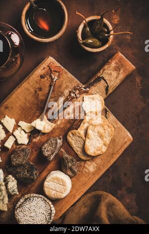 Assortimento di spuntini e antipasti per il concetto di vino rosso. Piatto di vari formaggi, cracker, carne affumicata, frutta e bicchiere di vino rosso su RU di legno Foto Stock