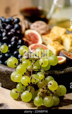 Antipasti di vino con diverse uve, fichi, noci, pane, miele e formaggio di capra su piatto di ceramica, da servire con bicchieri di vino rosso e bianco oltre Foto Stock