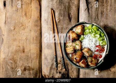 Pancia di maiale fritta alla griglia in ciotola con riso, sedano, peperoncino e cipollina con bastoncini sopra il vecchio fondo di legno. Posa piatta, copia spin Foto Stock