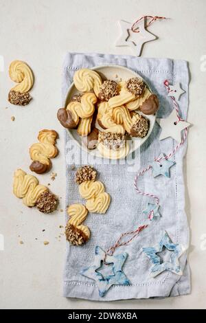 Biscotti frolla tradizionali fatti in casa di forme diverse con glassa al cioccolato e noci. Su piastra in ceramica con decorazioni a stelle di Natale su sfondo bianco Foto Stock