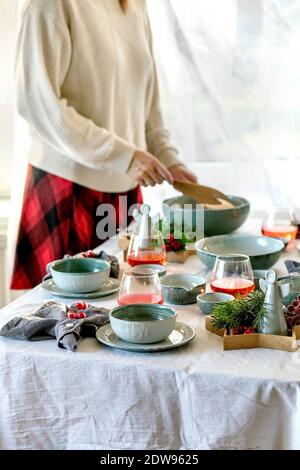 Rustico tavolo di Natale con stoviglie vuote artigianali in ceramica, piatti e ciotole, decorazioni d'angelo xmas su tovaglia bianca di fronte alla finestra Foto Stock