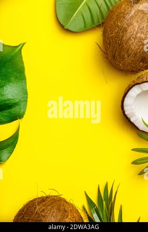 Noci di cocco e foglie tropicali su sfondo giallo, copyspace, laici piatta Foto Stock