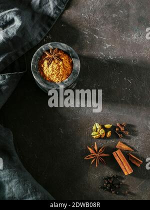 Polvere di masala indiana o pakistana e spezie sul retro nero. Piccola ciotola in marmo nero con crema di curry e masala mix di spezie, bastoncini di cannella Foto Stock