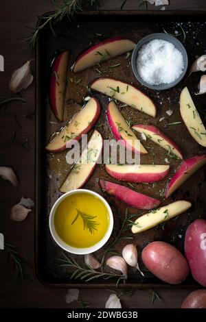 Spicchi di patate ricoperti di olio d'oliva e conditi con rosmarino e sale su una teglia da forno Foto Stock