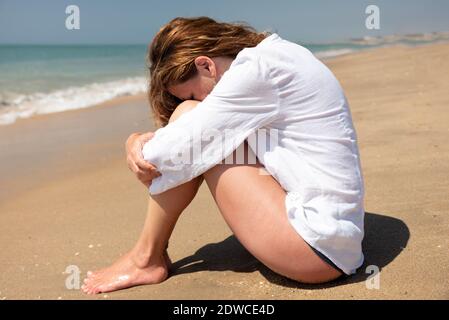 Donna seduta sulla riva che ricopre il viso con lei gambe Foto Stock