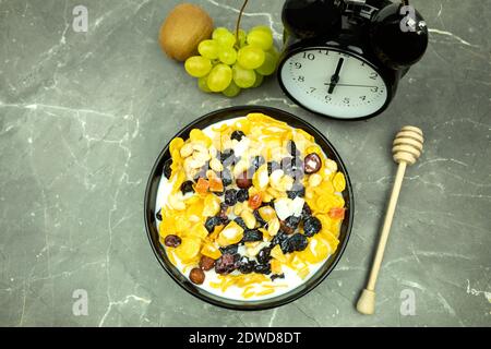 Un piatto con cornflakes come sfondo per il testo. La sveglia mostra sei ore. Fiocchi di miele e latte con frutta e latte. Colazione sana Foto Stock