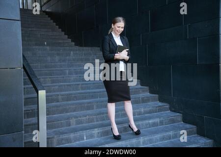 Donna di affari in un vestito con un diario si leva in piedi sopra i gradini Foto Stock