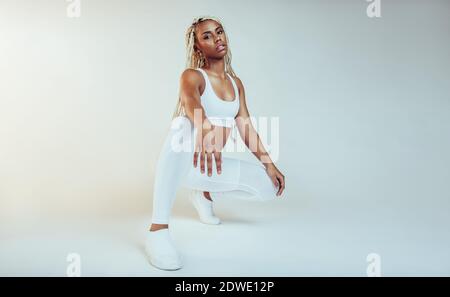 Donne afroamericane di fitness che si siedono e si rilassano dopo l'allenamento. Ritratto monocromatico di donna fitness su sfondo bianco. Foto Stock