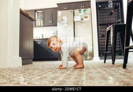 Carino bambino cercando di stare in piedi sui suoi piedi. Bambino in via di sviluppo in piedi sul pavimento a casa. Foto Stock
