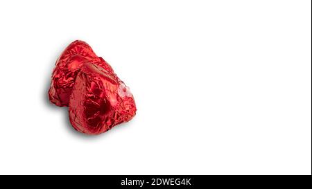 Dolce caramella a forma di cuore di cioccolato avvolto in papper di lamina rossa su sfondo bianco. Foto di alta qualità Foto Stock
