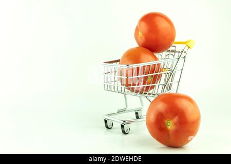 Pomodori freschi e un cestino della spesa in metallo su sfondo bianco. Mini cestino con pomodori freschi a sfondo chiaro. Pubblicità per un supermercato o g Foto Stock