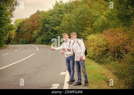 Inizia la grande avventura nella tua vita con hitchhiking. Compagnia amici viaggiatori hitchhiking a fondo natura strada. Vai vicino al bordo della città. Viaggiatori sulla loro strada. Amici hitchhikers in viaggio. Foto Stock