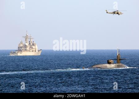 Handout foto datata 21 dicembre 2020 dell'elicottero MH-60R Seahawk, attaccato allo Squadrone Elicopter Sea Maritime (HSM 48), vola sopra il sottomarino missile guidato USS Georgia (SSGN 729) come il sottomarino che transita con l'incrociatore missilistico guidato USS Port Royal di classe Ticonderoga (CG 73) Sullo stretto di HormuzLa Marina statunitense sembra inviare un messaggio in Iran sotto forma di sottomarino missilistico guidato dotato di tremende forze d'artificio e forse di truppe speciali. Il sottomarino missilistico guidato USS Georgia di classe Ohio ha navigato nel Golfo Persico lunedì. Per la prima volta in Foto Stock