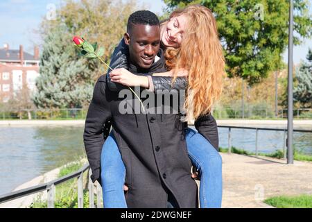 L'uomo nero africano e la donna caucasica rossa godendo di cavalcare con una rosa. Giovane coppia multirazziale che celebra il giorno delle valentine. Foto Stock