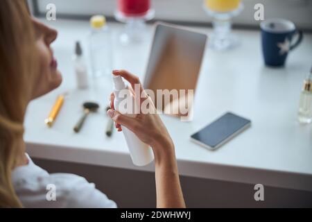 Giovane donna che si siede alla scrivania mentre si prende cura di il viso al mattino Foto Stock