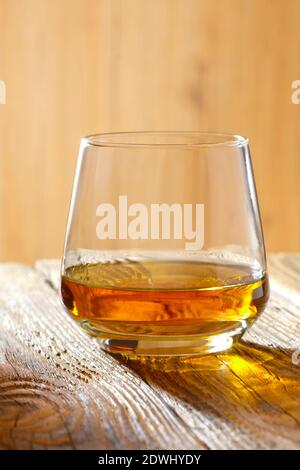 Sniffer di vetro con whiskey sulla tavola di legno in presenza di luce solare Foto Stock
