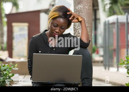 giovane donna che si siede all'esterno e che ha un aspetto pensivo su un computer portatile. Foto Stock