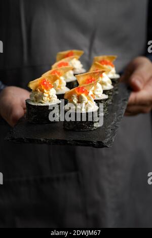 Sushi roll maki futo cibo giapponese su un piatto di pietra nera nelle mani di un cameriere. Primo piano Foto Stock