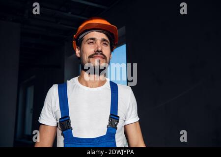 Un uomo regola un elmetto arancione sulla testa. Indossa una tuta blu Foto Stock