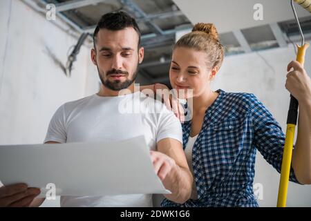 Una donna sorridente tiene un rullo in mano e abbraccia il marito. Guardano alla disposizione degli appartamenti Foto Stock