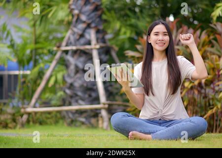 Donne asiatiche che tengono il tablet sul social network e lo shopping online via internet seduto nel parco cittadino Foto Stock