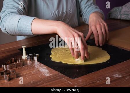 Giovane donna che prepara i biscotti di natale su carta da forno nera sopra tabella Foto Stock