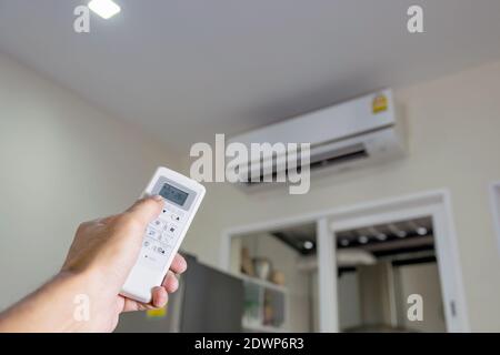 Tenere il telecomando con la mano per controllare il climatizzatore nella stanza. Foto Stock