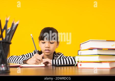 Bambino asiatico giovane, scrittura della ragazza thailandese e nota sul tavolo con sfondo giallo Foto Stock