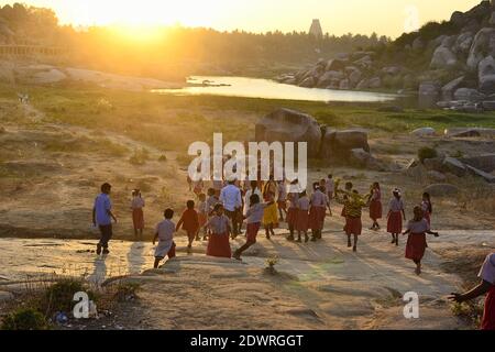 Hampi, India - 23 dicembre 2016: Un gruppo di bambini indiani gioca sulle rocce. I bambini si divertono con i raggi del sole luminosi al tramonto. Foto Stock