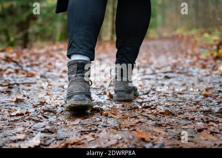 Primo piano di escursionisti che camminano lungo il percorso della foresta umida. Persona con scarpe da trekking sporche sul sentiero all'aperto. Foto Stock